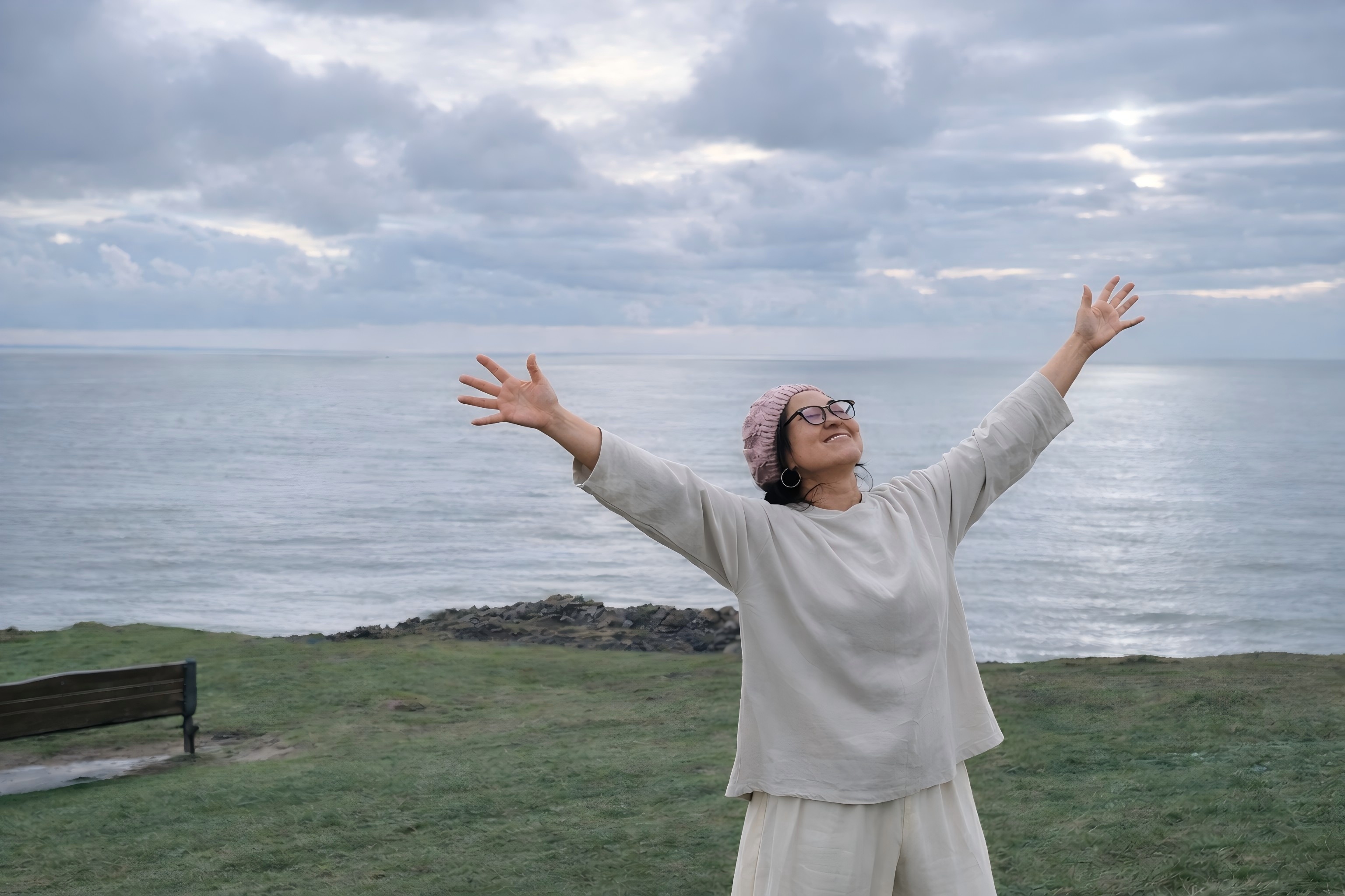 A woman opening her arms beside the sea during a Tai Chi for Women practice